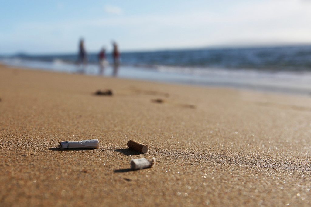 Cigarette butts on the beach with three people off in the distance.